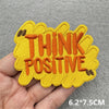 Yellow embroidered patch with orange text that reads THINK POSITIVE, shown being held in a hand.