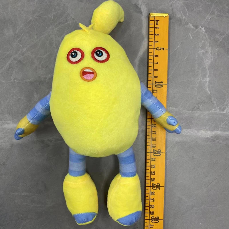 A yellow plush toy resembling a bird with large eyes and an open mouth, standing next to a ruler.