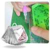 A silver diamond art storage bag with a pink seal is shown next to a green grid of beads and a pink liquid dispenser.