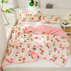 A pink and white quilted summer blanket with a floral pattern is displayed on a white surface next to pillows.