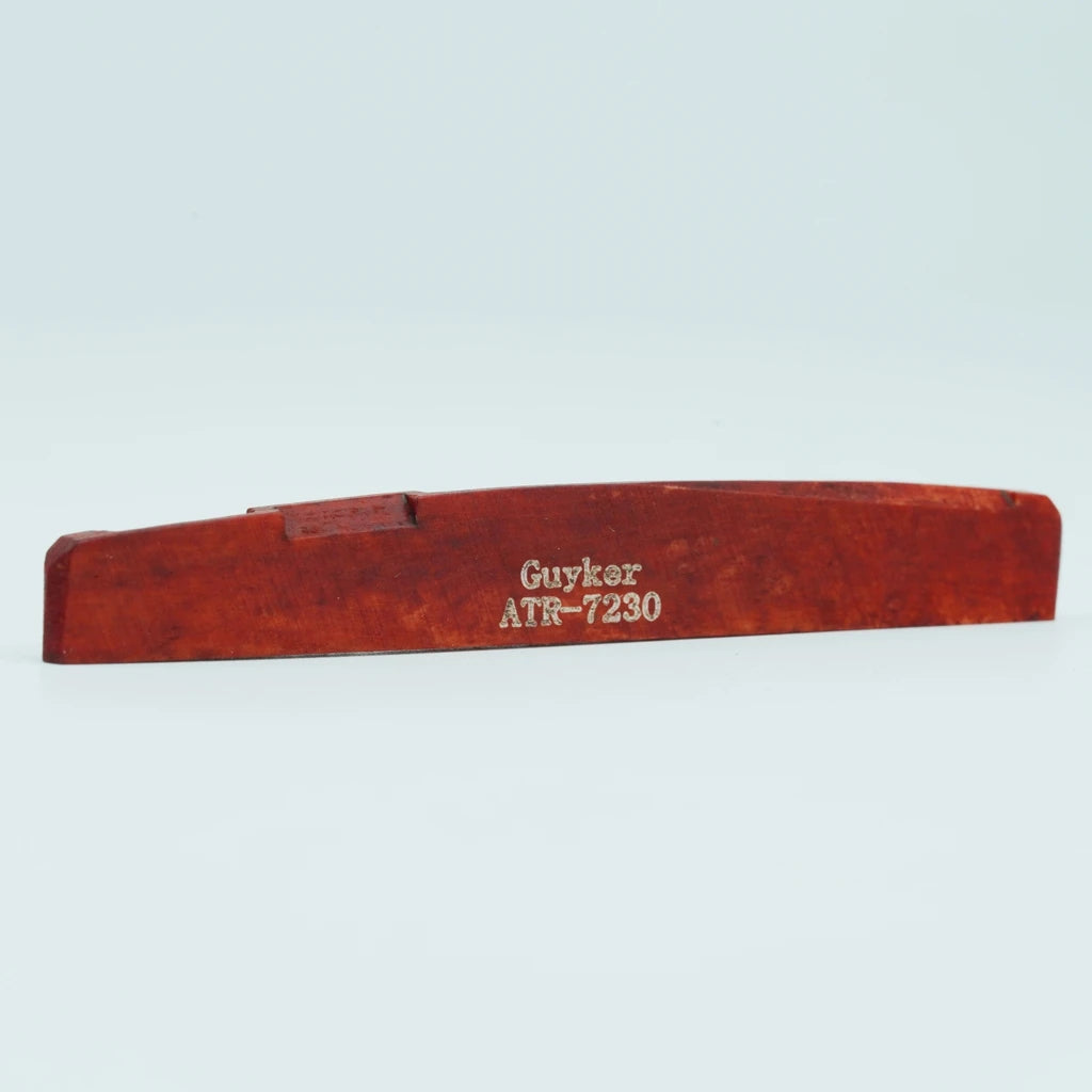 A wooden acoustic guitar bridge saddle with the name Guyker ATR-7230 engraved on it.