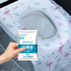 A hand holds a package of disposable toilet seat covers for travel and public restrooms against a light blue patterned surfac