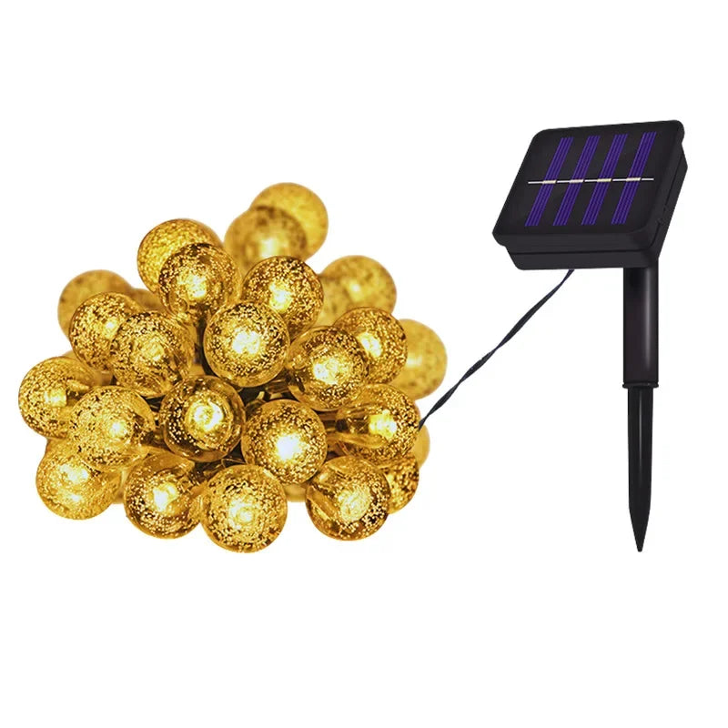 A cluster of golden crystal globe string lights connected by a wire, next to a black solar panel light fixture.