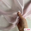 A hand is gently folding a piece of light pink mulberry silk chiffon fabric.