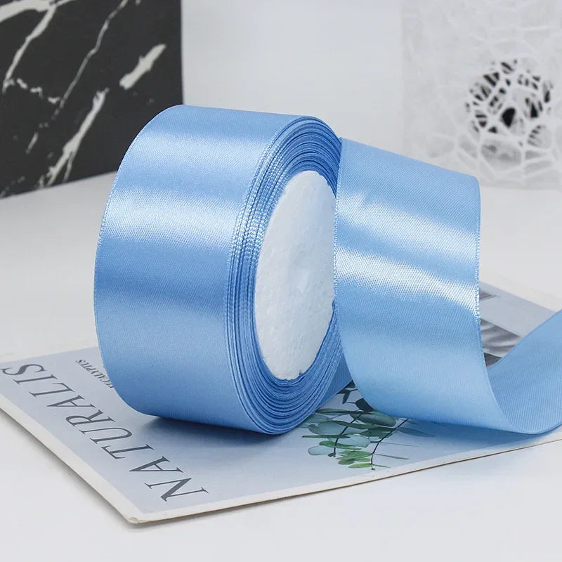 A roll of light blue satin ribbon used for gift wrapping or DIY crafts, shown next to a piece of paper.