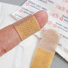 A finger holds a square adhesive bandage, showing its texture and layered design against a white background.