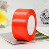 A roll of bright orange satin ribbon used for gift wrapping or DIY crafts, lying on a white surface.