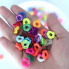 A hand holds a collection of colorful acrylic spacer beads in various shapes and colors for jewelry making.