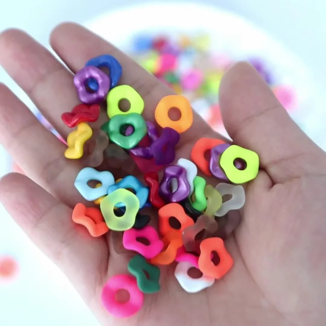 A hand holds a collection of colorful acrylic spacer beads in various shapes and colors for jewelry making.