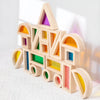 A wooden building block structure shaped like a rainbow, featuring various colored acrylic blocks.
