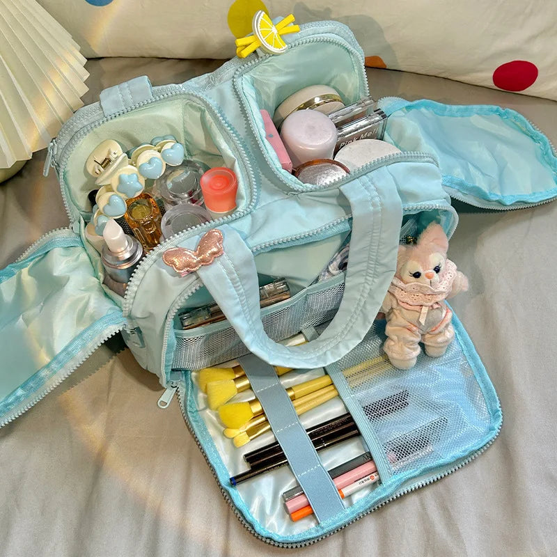 A light blue cosmetic travel organizer with multiple compartments and a clear lid is shown on a soft surface.
