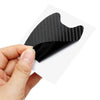 A hand holds a black carbon fiber door handle protector film, showing its textured surface.