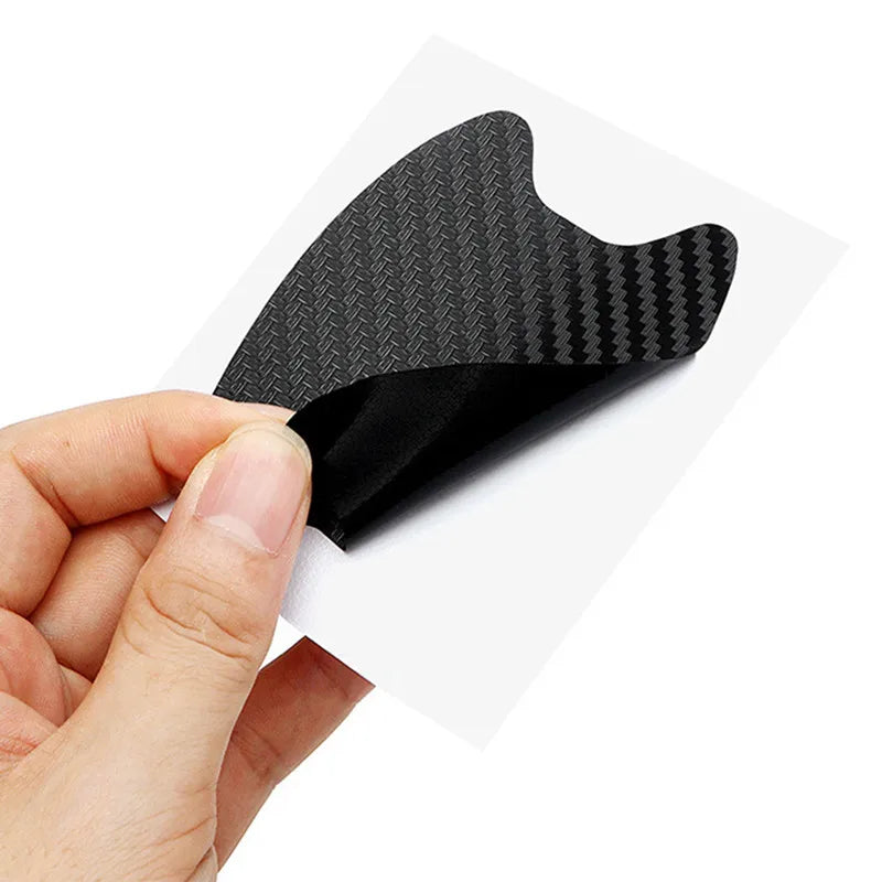 A hand holds a black carbon fiber door handle protector film, showing its textured surface.