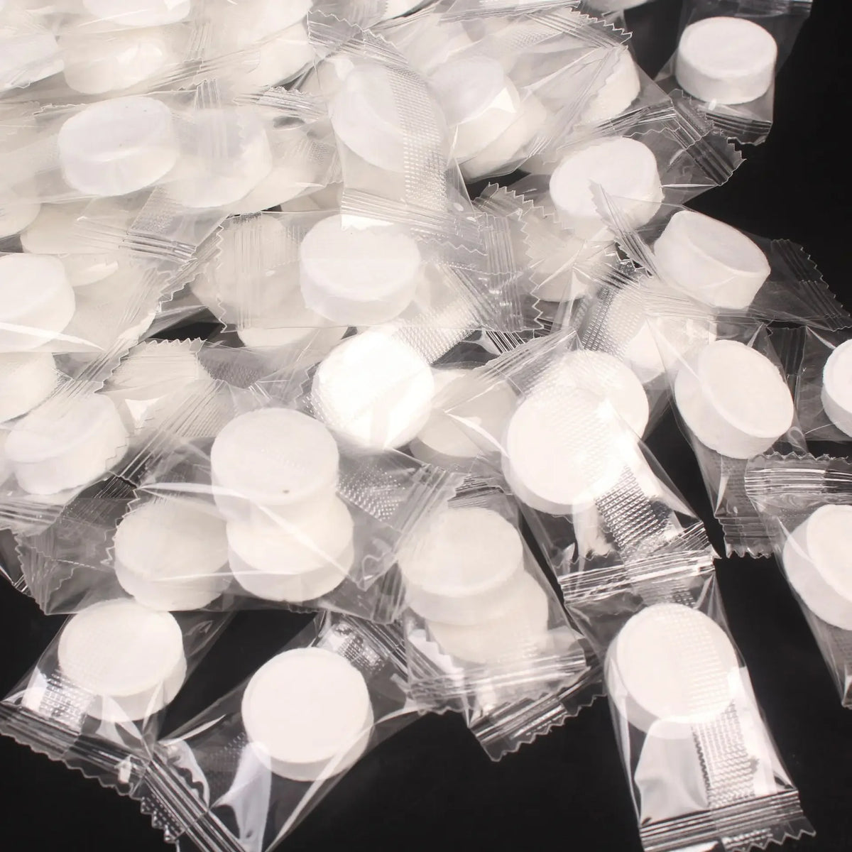 A pile of small, white, compressed cleansing towels packaged in clear plastic.