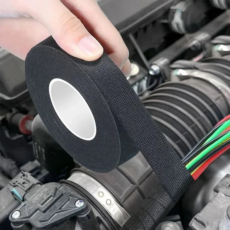 Eine Hand hält eine Rolle schwarzes hitzebeständiges Isoliermaterial (elektrisches Klebeband) in der Nähe einer Motorkomponen
