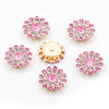 A collection of pink and clear rhinestone flowers, some gold-toned, arranged on a white background.