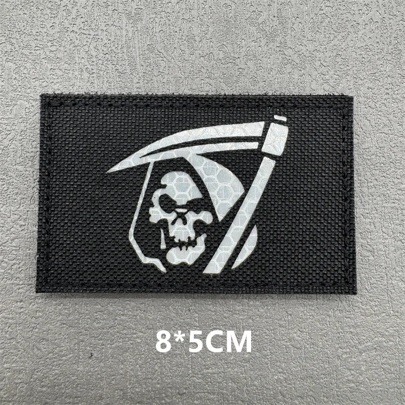 Black embroidered patch featuring a white skull and crossbones design with a stylized sword above it.