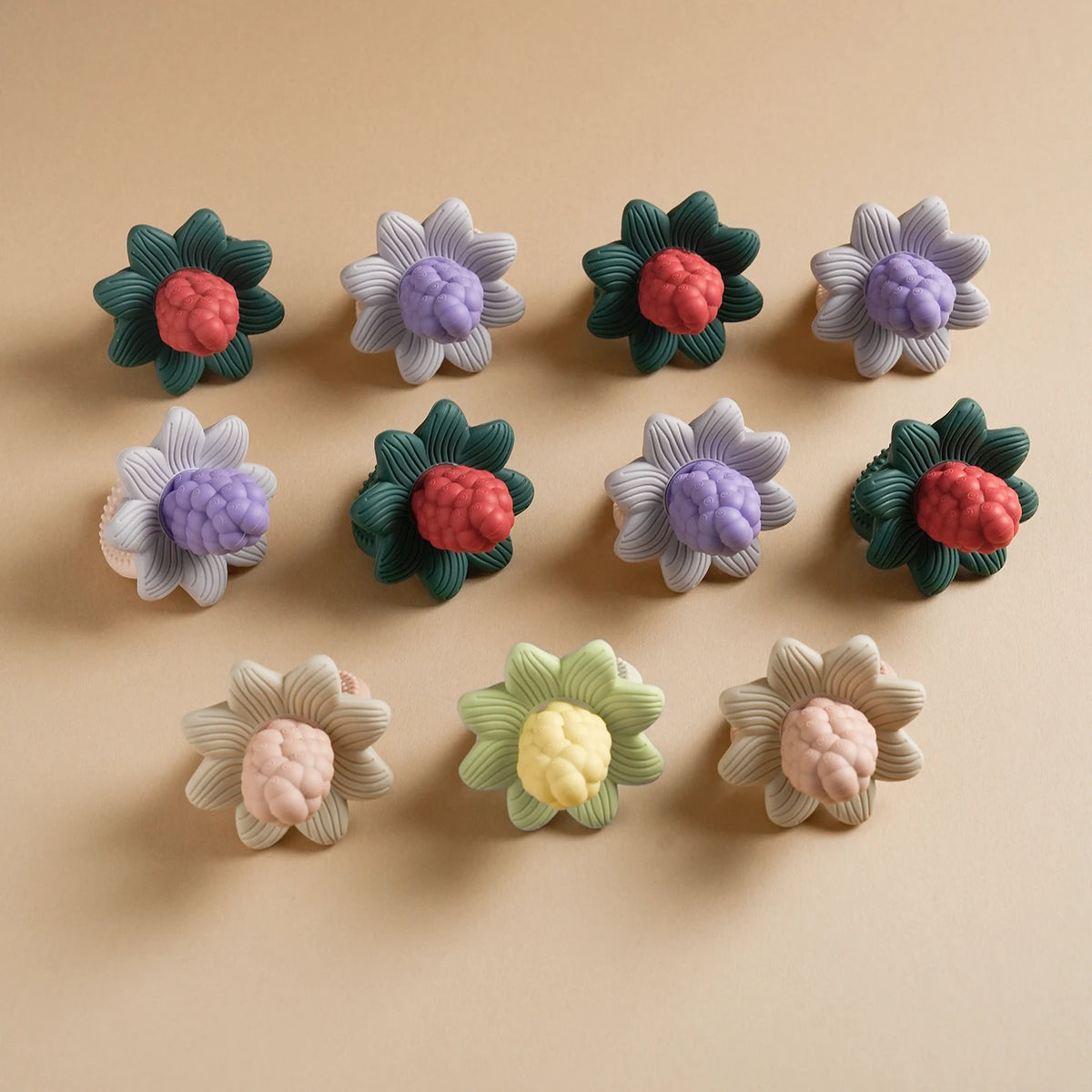 A collection of silicone baby teether toys shaped like flowers and grapes in various shades of purple, green, pink, and laven