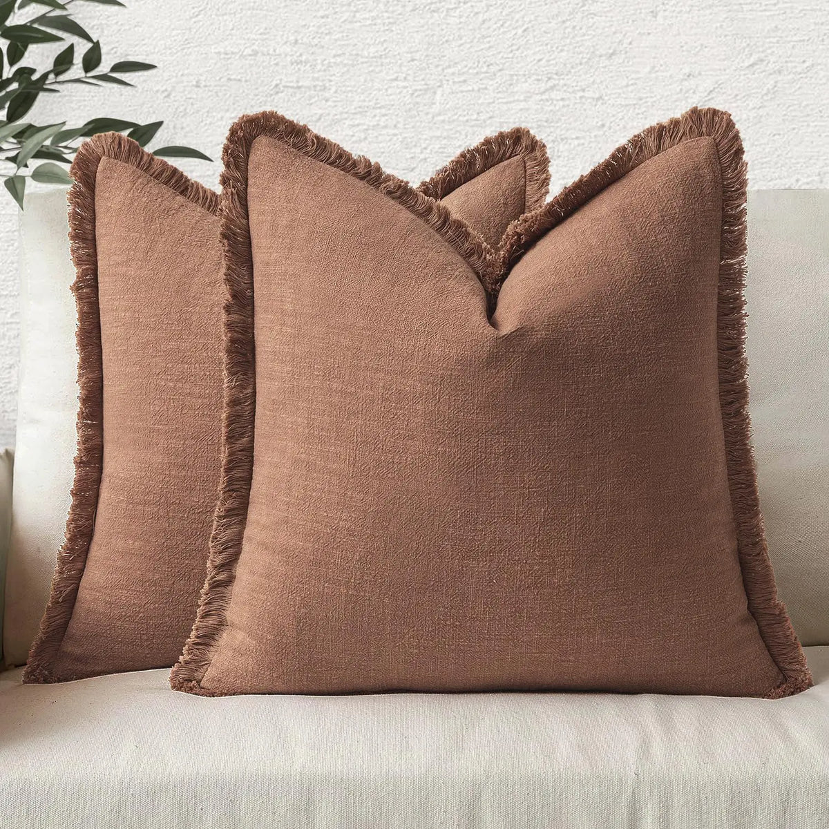 A tan boho fringe throw pillow cover with a natural linen texture resting on a light-colored sofa.
