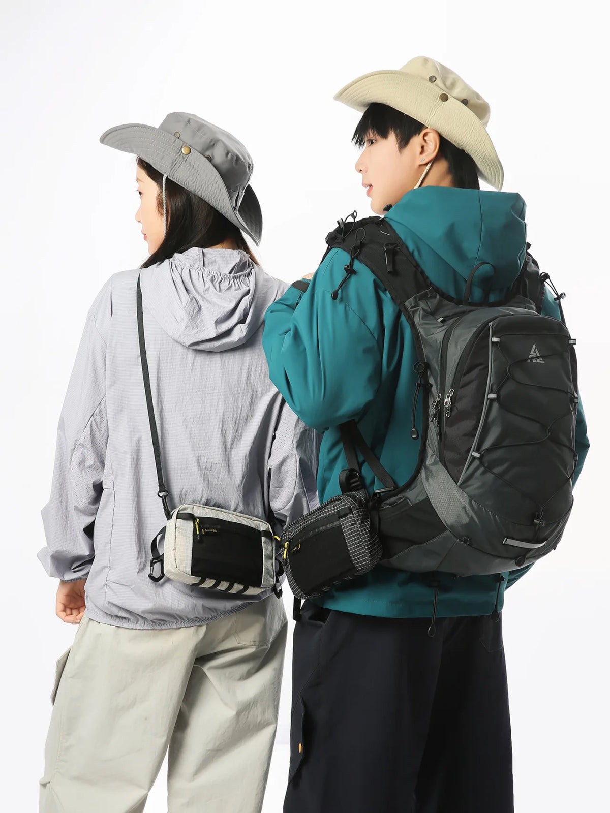 A person wearing a teal jacket and a beige hat is carrying a black tactical backpack.