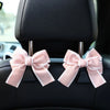 Pink bow-shaped car seat back hooks with storage attached to a black car seat.