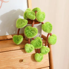 A potted plant made of soft green faux leaves resembling a pothos, displayed on a wooden surface.