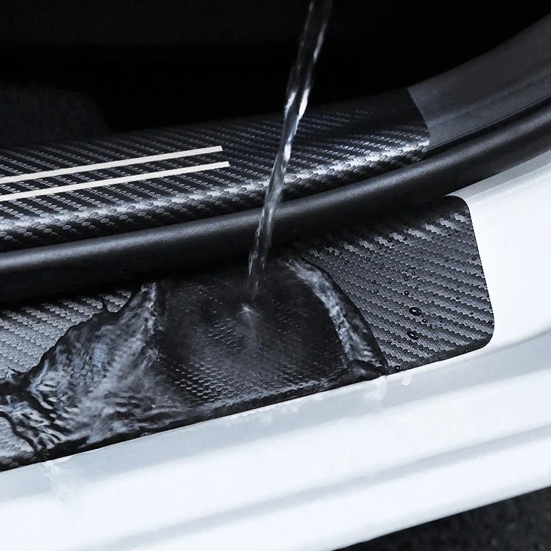 Close-up of a carbon fiber door sill protector sticker being wet with water on a white car body.