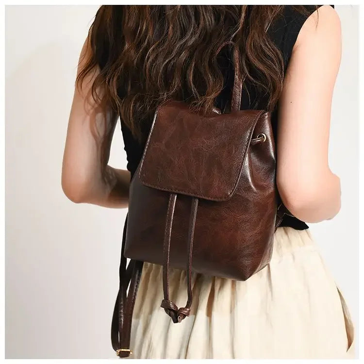 Mini sac à dos en cuir marron avec cordon, porté par une personne aux longs cheveux noirs et un haut de couleur claire.