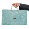 A teal water-resistant laptop briefcase with a stitched cat face design and silver chain handles is held by a hand.
