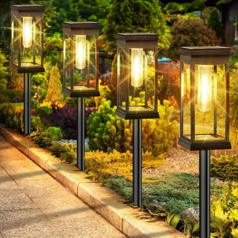 Four tall solar path lights with warm glow illuminate a garden pathway and landscaping.