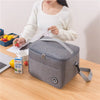A woman holds a gray thermal insulated lunch bag with an adjustable strap on a wooden table.