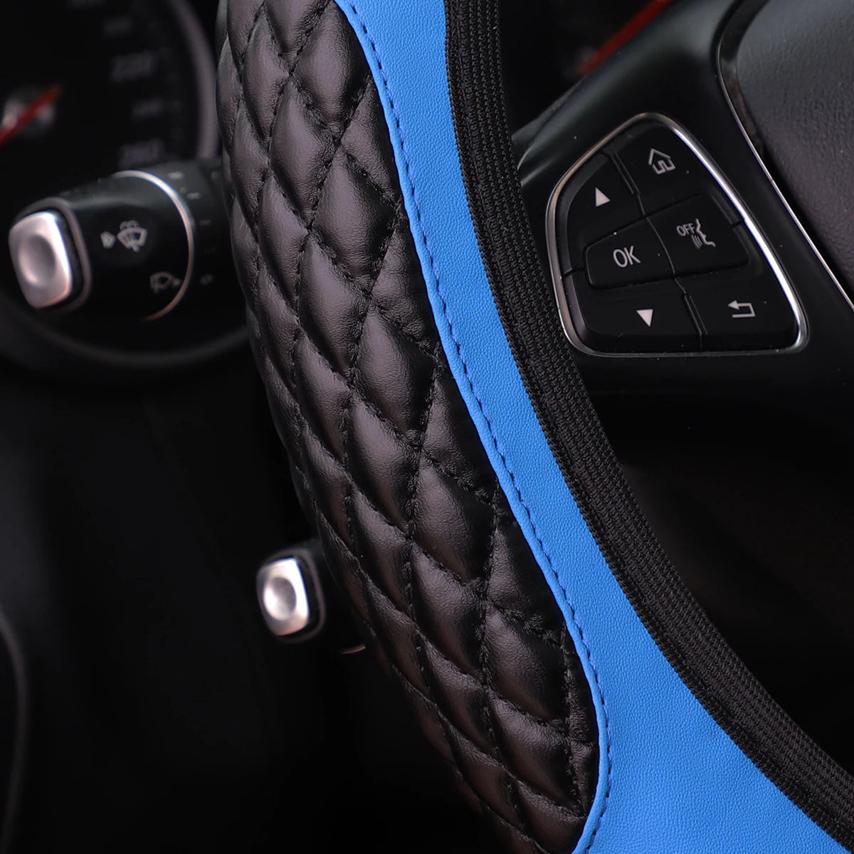 Close-up of a black quilted steering wheel cover with a bright blue accent stitching and controls.