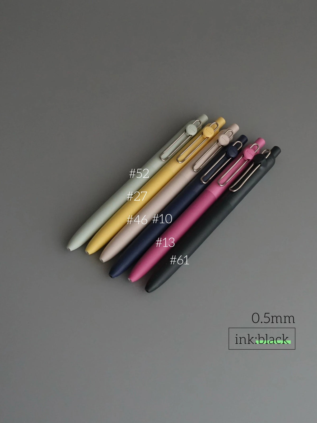 A collection of Uni ZENTO Quick-Dry Gel Pens in various colors and finishes, laid diagonally on a gray background.