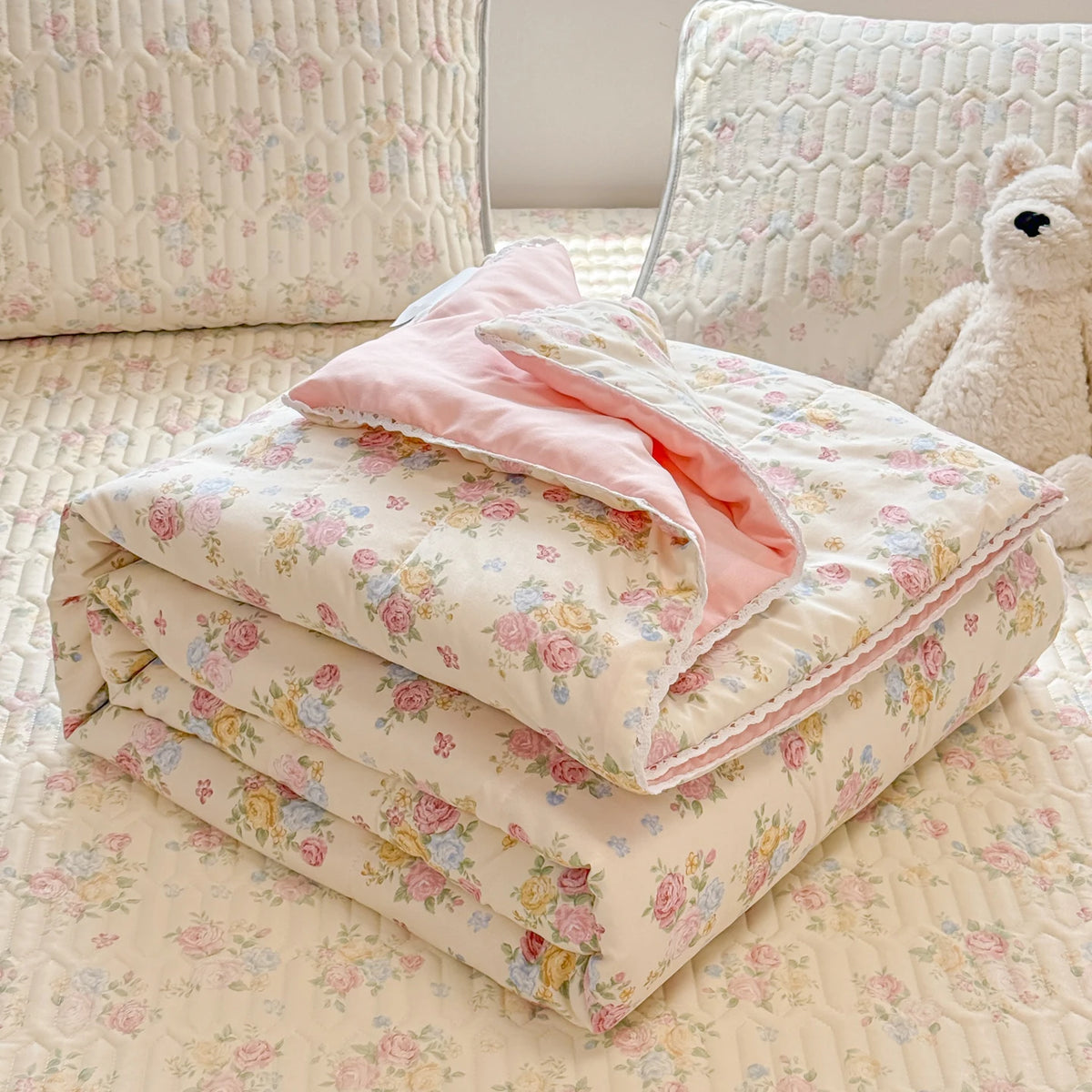 A stack of pink and cream lace-trimmed breathable summer duvet covers resting on a quilted fabric surface.