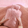 Eine Person hält eine große rosa Kunstfell-Heißwasserflasche vor einem rosa gestrickten Stoffhintergrund.