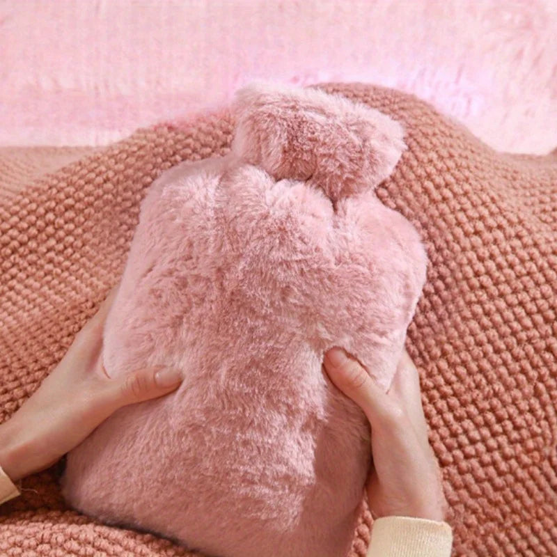 Eine Person hält eine große rosa Kunstfell-Heißwasserflasche vor einem rosa gestrickten Stoffhintergrund.