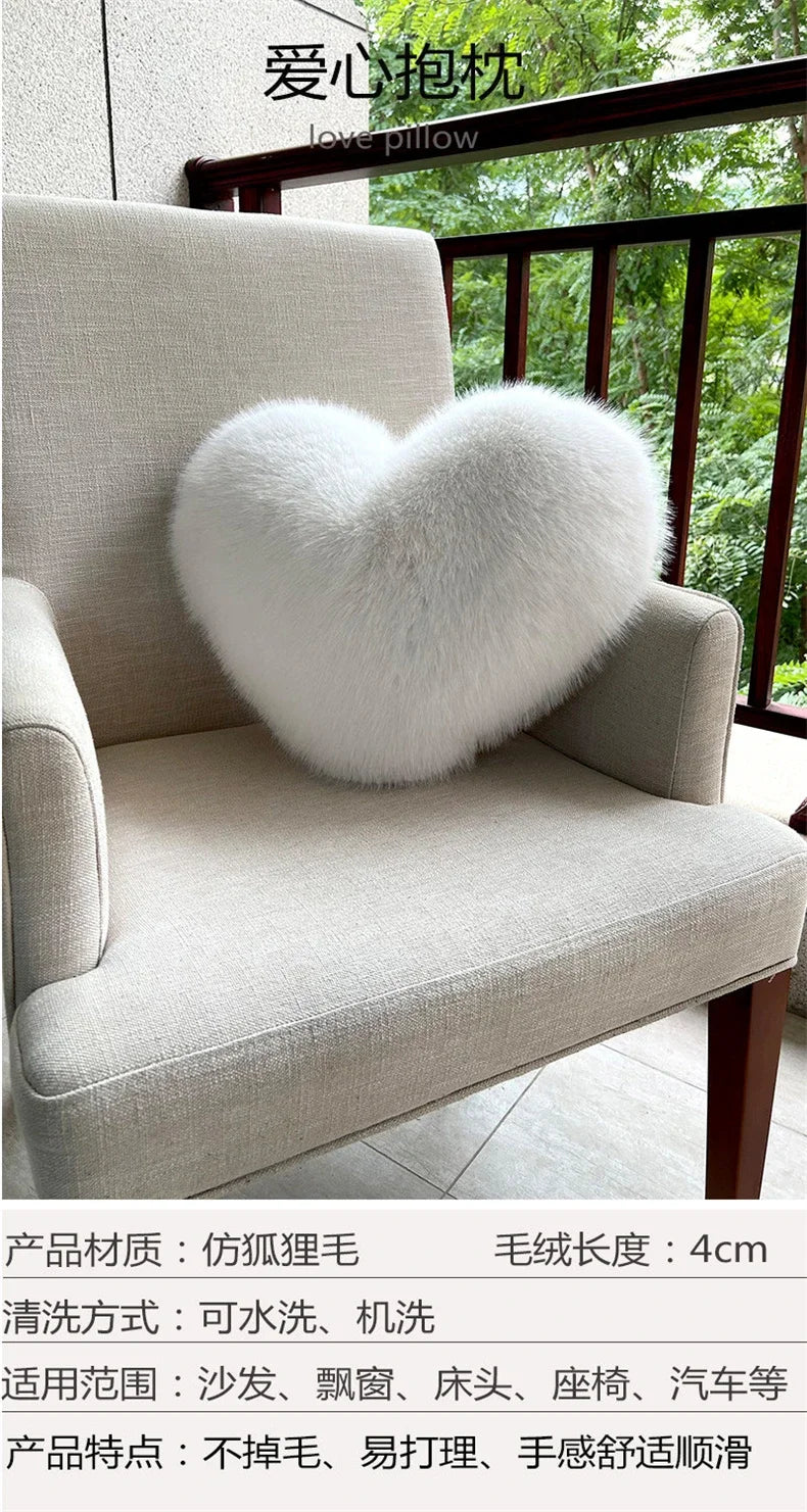 A fluffy white heart-shaped pillow resting on a light beige armchair with a wooden railing and greenery in the background.