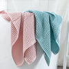 A set of two folded waffle weave bath towels in pink and light blue hanging on a white rack.