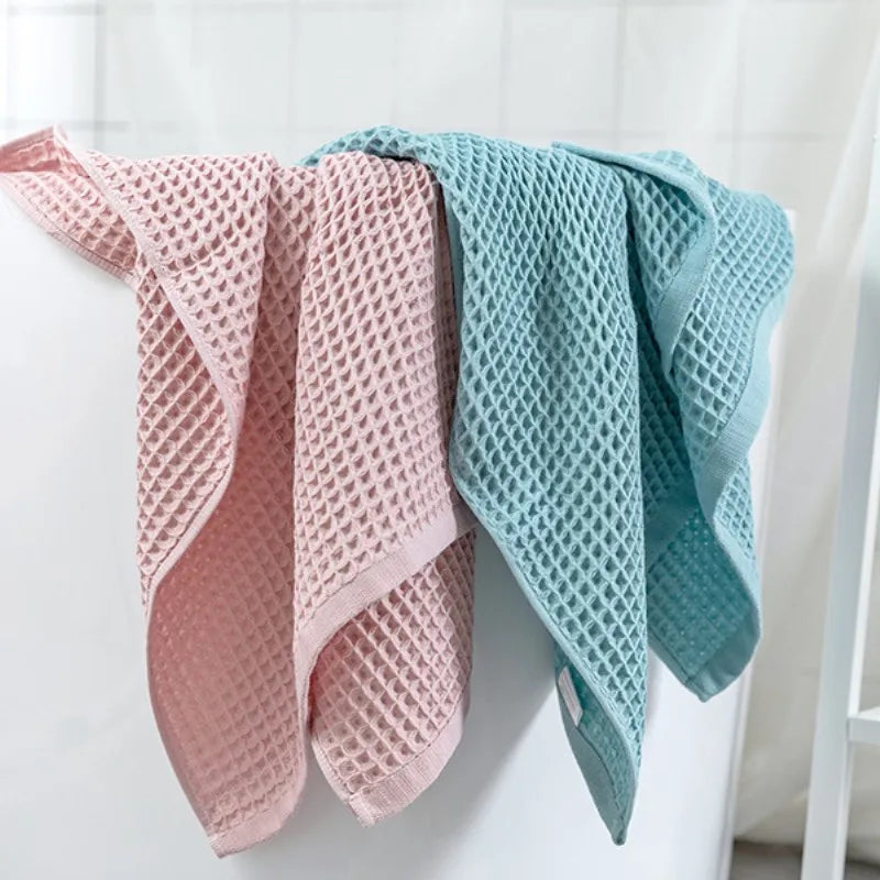 A set of two folded waffle weave bath towels in pink and light blue hanging on a white rack.