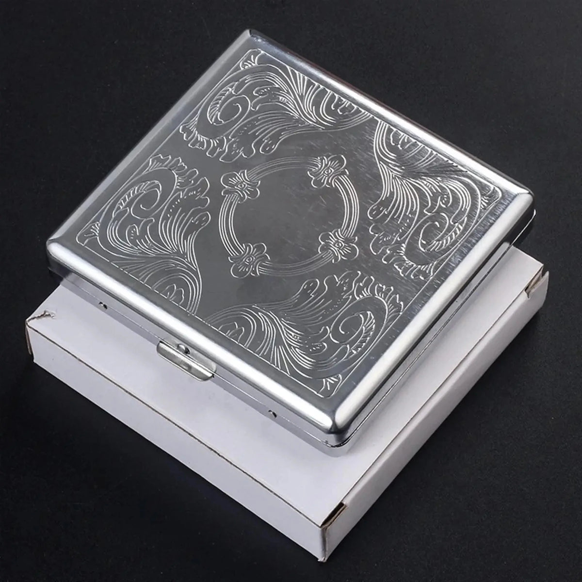Classic stainless steel cigarette case with an embossed swirling pattern resting in its white presentation box.