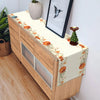 A wooden buffet cabinet decorated with a fall harvest table runner featuring orange pumpkins and autumn leaves.