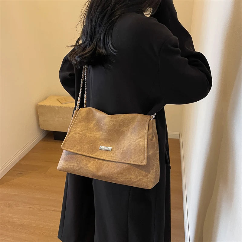 امرأة ترتدي معطفًا أسود تحمل حقيبة كتف جلدية بلون التان بسلسلة ذهبية.