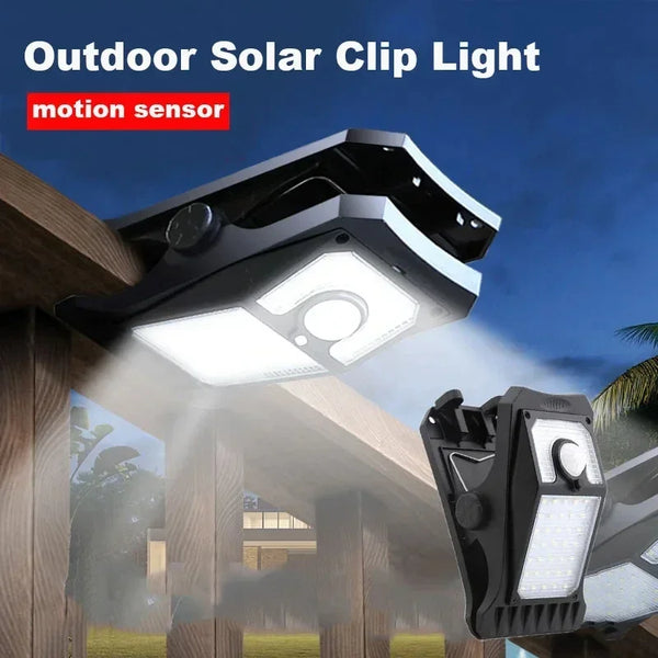 Luz solar de clip con sensor de movimiento montada en una cerca de madera, iluminando el área.