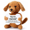 A handmade crochet dog doll in brown yarn with a white card that reads You're pawsome Just the way you are