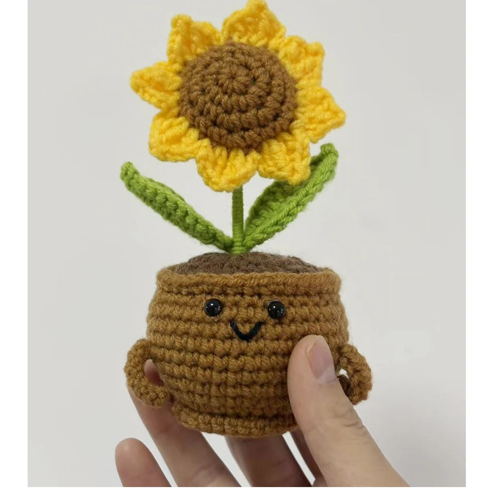 Handcrafted crochet sunflower with green leaves growing out of a brown pot being held by a hand