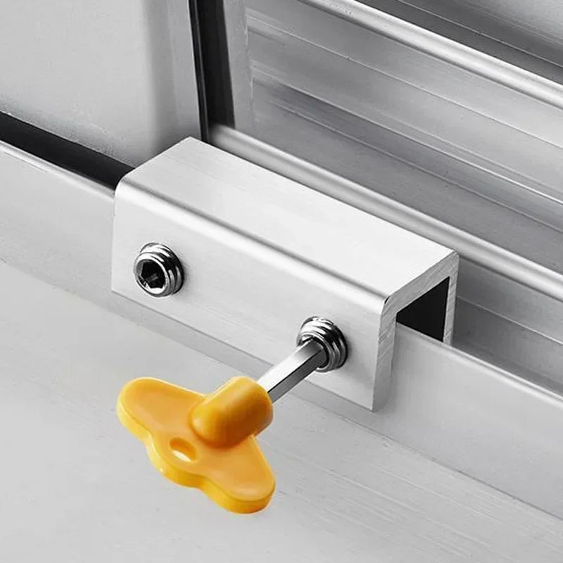 A silver aluminum alloy sliding window lock with a yellow plastic hex key is installed in a white window frame.