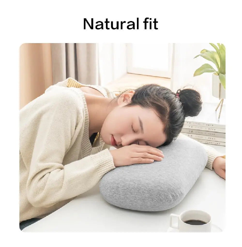 A woman rests her head on a gray memory foam travel neck pillow with a beige cover.