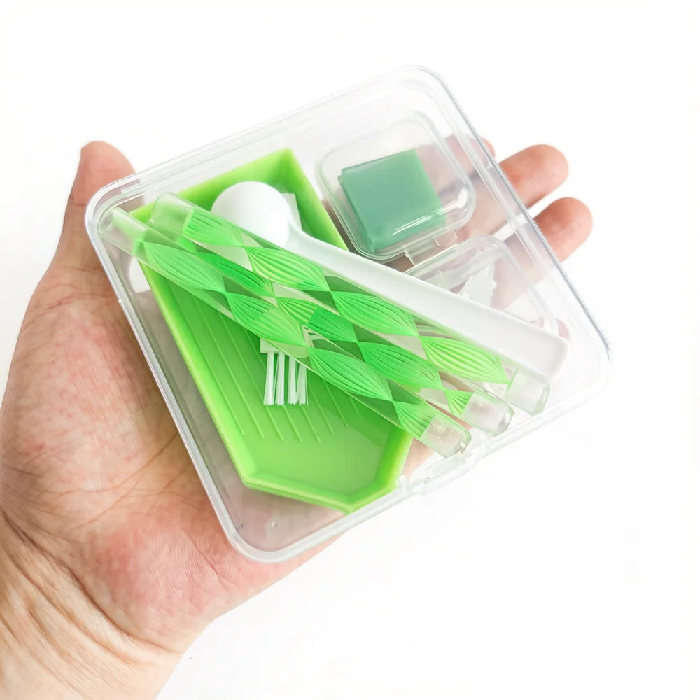 A clear plastic storage box containing a diamond painting accessory kit with green tools and a white bead.