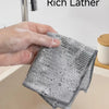 A hand is holding a textured, gray cleaning cloth with fine pores and rich lather over a kitchen sink.