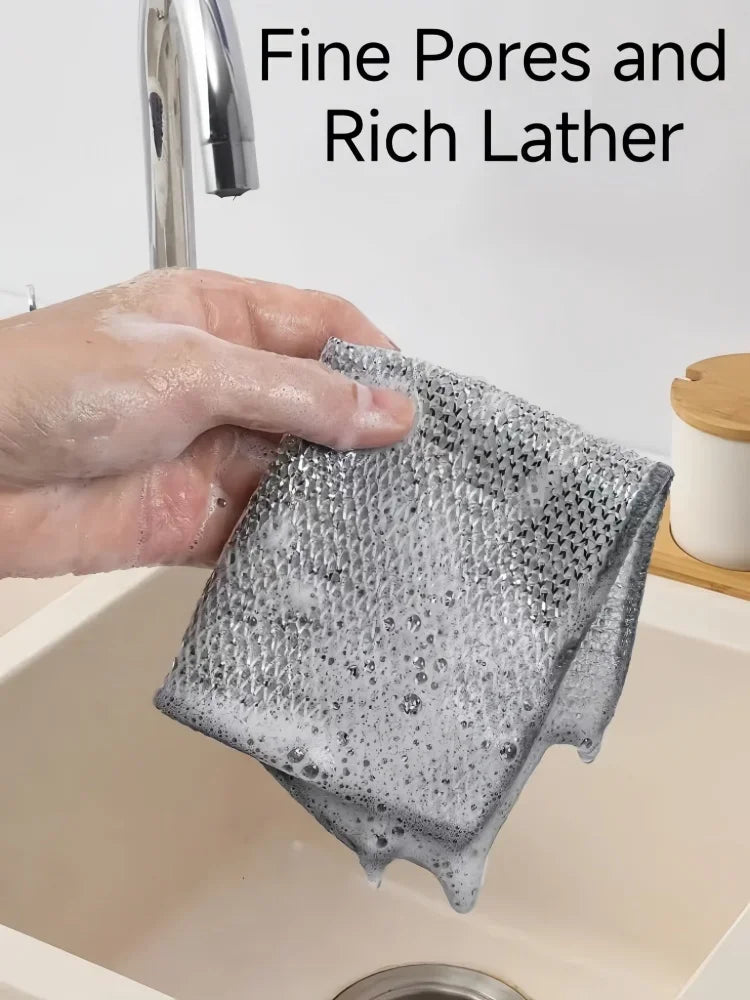 A hand is holding a textured, gray cleaning cloth with fine pores and rich lather over a kitchen sink.